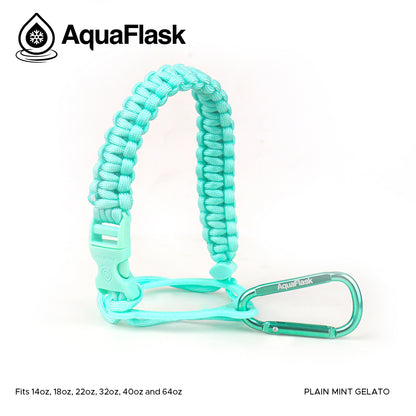 Accesorio de asa de paracord Aquaflask presentado sobre un fondo blanco con el logotipo de Aquaflask. El accesorio está fabricado con paracord firmemente tejido que forma un asa corta. Incluye una hebilla plástica de liberación lateral, un lazo ajustable que se coloca alrededor del cuello de la botella y un mosquetón metálico negro para su sujeción. El producto está etiquetado como compatible con botellas Aquaflask de 14 oz, 18 oz, 22 oz, 32 oz, 40 oz y 64 oz.