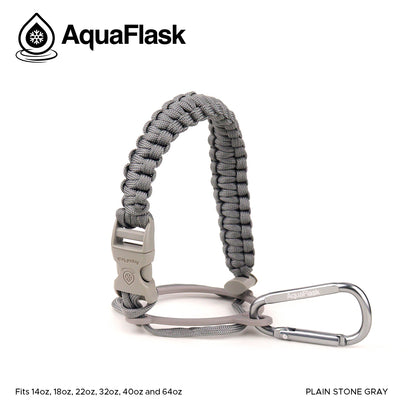 Accesorio de asa de paracord Aquaflask presentado sobre un fondo blanco con el logotipo de Aquaflask. El accesorio está fabricado con paracord firmemente tejido que forma un asa corta. Incluye una hebilla plástica de liberación lateral, un lazo ajustable que se coloca alrededor del cuello de la botella y un mosquetón metálico negro para su sujeción. El producto está etiquetado como compatible con botellas Aquaflask de 14 oz, 18 oz, 22 oz, 32 oz, 40 oz y 64 oz.